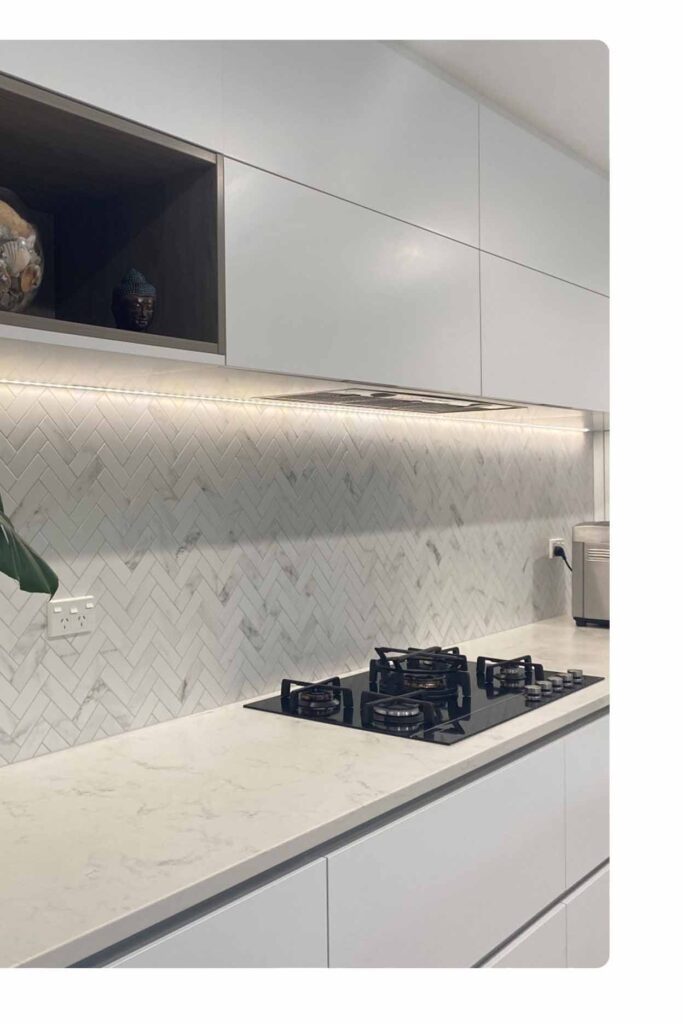 Modern herringbone marble kitchen splashback with white cabinetry and LED lighting by Badel Kitchens Sydney