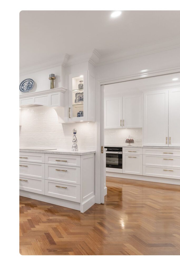 Classic white kitchen renovation in Western Sydney featuring shaker cabinetry, herringbone timber floors, and gold hardware.